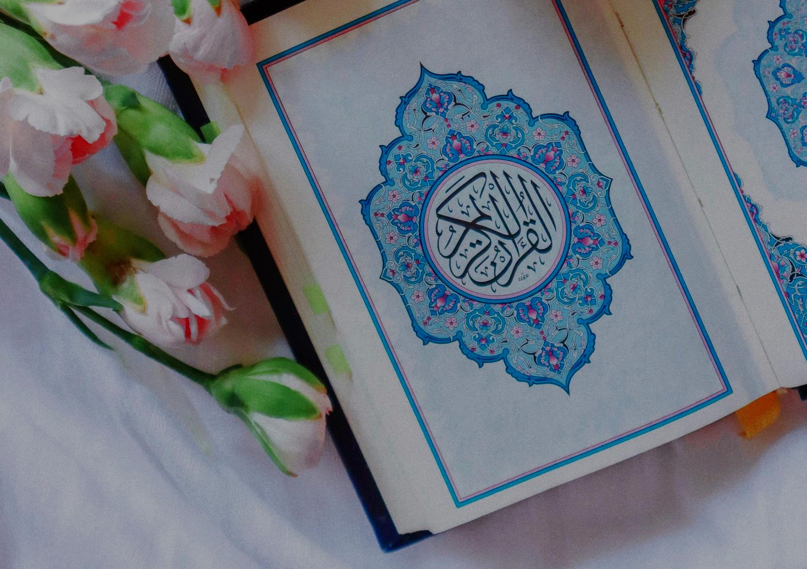 Mushaf Al-Qur'an terbuka dengan ornamen kaligrafi dikelilingi bunga